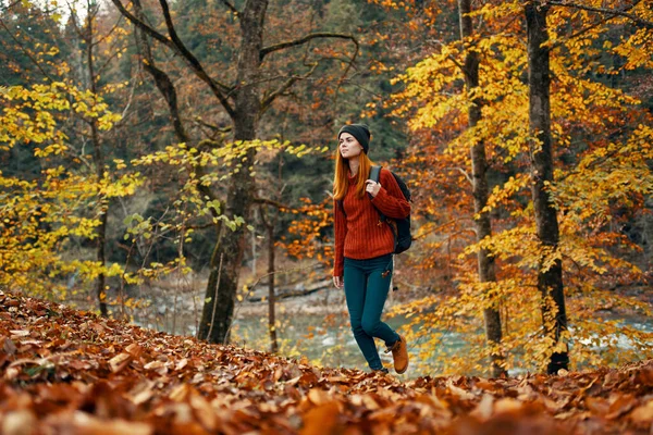 Woman tourist walks through the park in autumn with a backpack on her back and tall trees landscape river lake — Stock Photo, Image