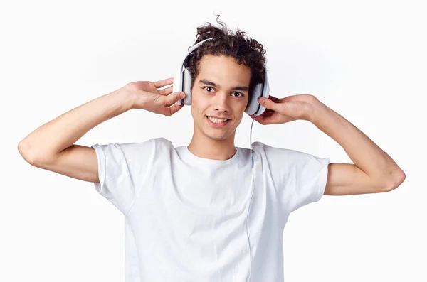 Tipo de pelo rizado feliz en auriculares y en una camiseta blanca escucha música y sostiene sus manos cerca de su cara — Foto de Stock