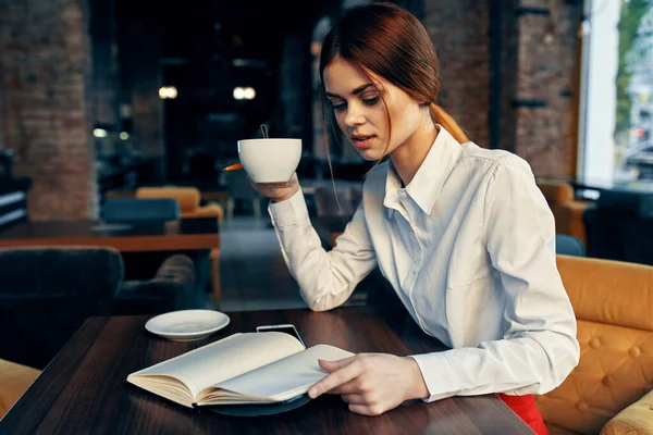 女人们穿着裙子衬衫，手拿着咖啡杯和记事本坐在餐桌旁 — 图库照片