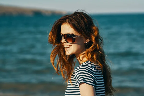 Portret rudej kobiety w okularach przeciwsłonecznych w górach nad morzem i uśmiech śmiejący się z podróży — Zdjęcie stockowe