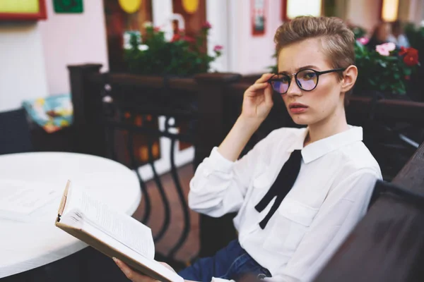 Femme à la table avec livre à lunettes à main sur le visage du café intérieur rue été — Photo