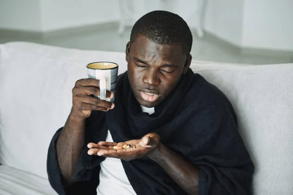 Африканский человек с таблетками в руке проблемы со здоровьем и чашку воды — стоковое фото