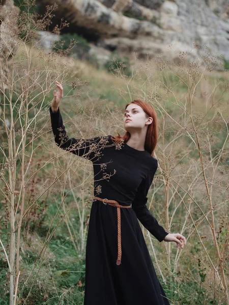 Mulher de cabelos vermelhos em um vestido preto estão andando sobre a natureza no outono na floresta — Fotografia de Stock