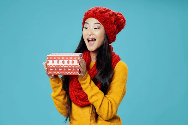 Glücklich asiatische Frau mit Geschenk-Box in den Händen und warmen Schal Kopfbedeckung Pullover blauer Hintergrund — Stockfoto