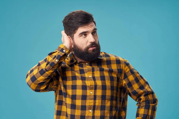 Hombre guapo con barba y camisa a cuadros toca su cabeza con su mano — Foto de Stock