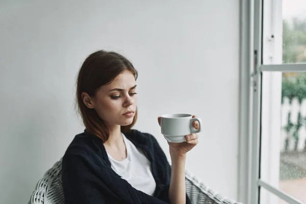 Женщина сидит в кресле с чашкой кофе возле окна интерьера отдыха — стоковое фото