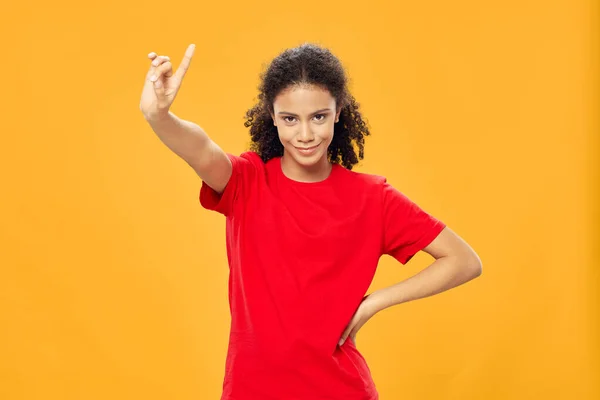 Vrouw met krullend haar in een rood t-shirt gebaren met een hand op een gele achtergrond — Stockfoto