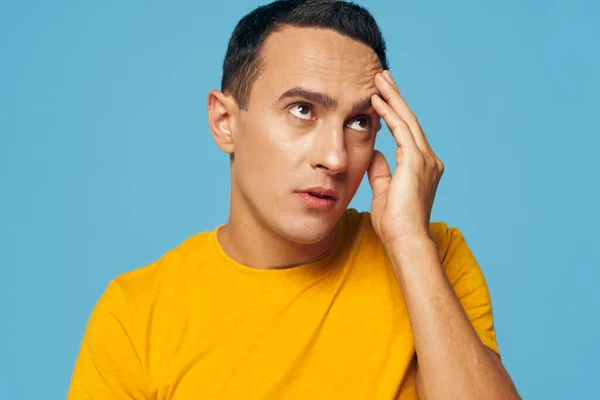 Homem emocional em uma camiseta amarela e segurando sua cabeça azul fundo — Fotografia de Stock
