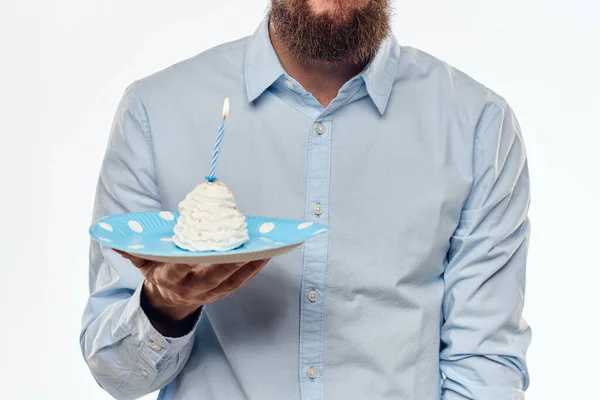 케이크 접시를 들고 밝은 배경 배경에 파란 셔츠를 입은 남자 생일 파티 모자를 쓴 남자 — 스톡 사진