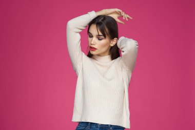 Kırmızı dudaklı, makyajlı beyaz bluzlu, uzun saçlı, pembe arka planlı bir kadın.