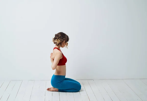 En kvinna i blå leggings sitter på ett ljust golv inomhus och håller händerna bakom ryggen — Stockfoto