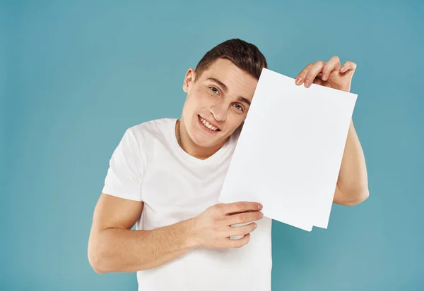 Cara feliz mostra um panfleto em sua mão em um fundo azul publicidade mockup — Fotografia de Stock