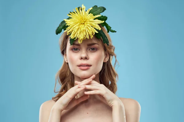 Kobiety z żółtym kwiatem na głowie na niebieskim tle nagie ramiona portret — Zdjęcie stockowe