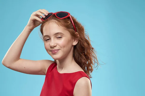 Menina com cabelo encaracolado óculos de sol vestido vermelho e infância divertido fundo azul — Fotografia de Stock