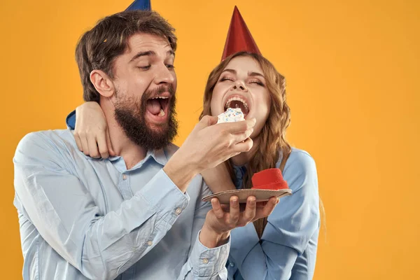 Aniversário festa homem e mulher em um boné com um bolo em um fundo amarelo vista cortada — Fotografia de Stock