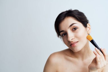 Güzel esmer, çıplak omuzlu. Çekici görünmek için yüzüne makyaj yapıyor.