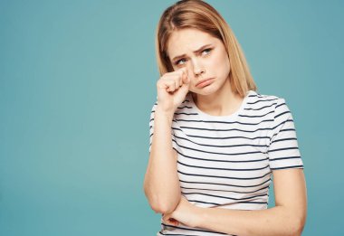 Mavi arka planda ağlayan ve elleriyle yüzüne dokunan sevimli sarışın kadın.