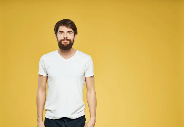 Retrato de un hombre sobre un fondo amarillo con una camiseta blanca y pantalones oscuros — Foto de Stock