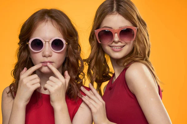 Cheerful mom and daughter wearing sunglasses lifestyle friendship family yellow background studio — Stock Photo, Image