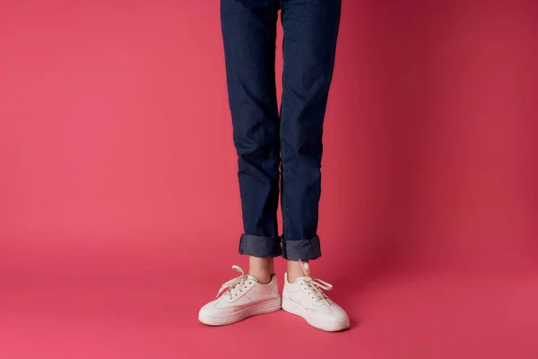 Donna gambe jeans bianco sneakers strada moda studio rosa sfondo — Foto Stock