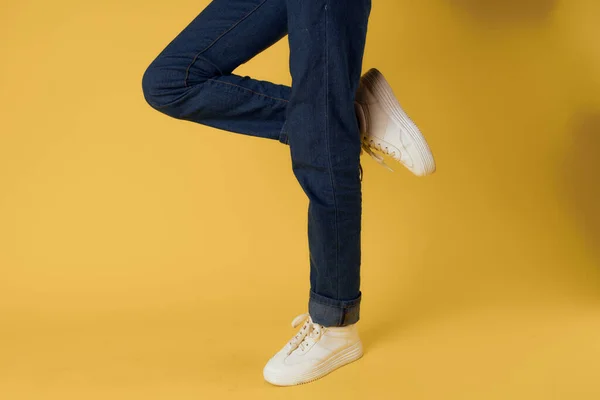 Voet gebaar witte sneakers mode jeans straat stijl gele achtergrond — Stockfoto