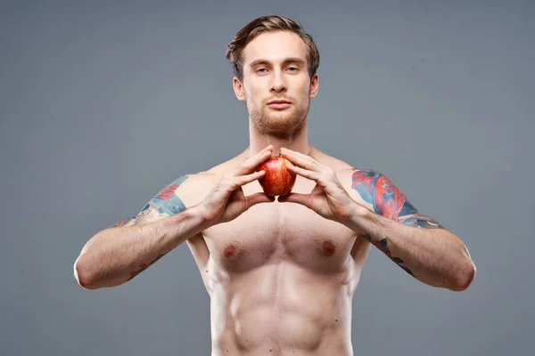 Atleta masculino con una manzana en las manos y cubos de tatuaje en el estómago prensa bíceps — Foto de Stock