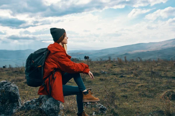 Viaggiatore In giacca rossa, cappelli con zaino si siede su una pietra in montagna nella natura — Foto Stock