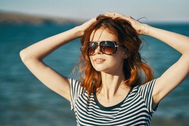 Deniz kenarındaki kumsalda bir yaz gezgini elleriyle kafasına dokunuyor.