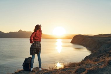 Elleri havada neşeli bir kadın gün batımına bakıyor. Seyahat özgürlüğü.
