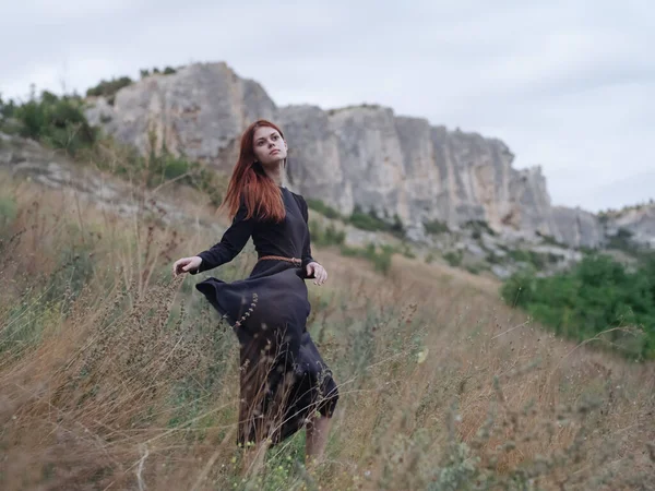 Viajante na floresta em um prado nas montanhas vestido preto cabelo vermelho — Fotografia de Stock