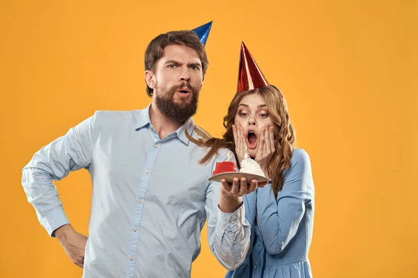 En man med en födelsedagstårta i sina händer och i en hatt på en gul bakgrund på sin födelsedag — Stockfoto
