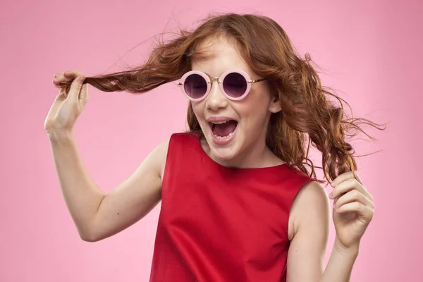 Mädchen mit lockigem Haar dunkle runde Brille Spaß rotes Kleid rosa Hintergrund — Stockfoto