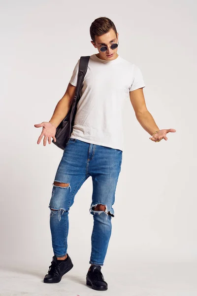 En man med ryggsäck på ryggen i jeans t-shirt full längd sneakers och glasögon på ansiktet — Stockfoto
