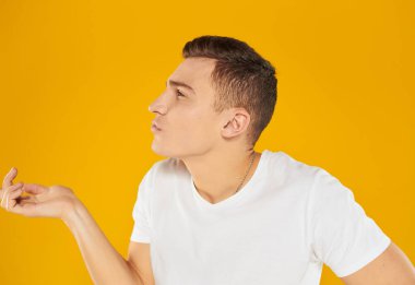 Sarı arka planda beyaz tişörtlü duygusal adam ellerini sürpriz modele doğru uzatıyor.
