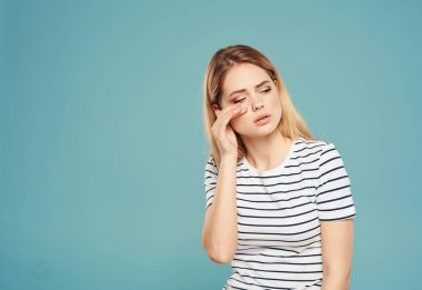 Kafası karışmış bir kadın, mavi bir arka plan modeli üzerinde elleriyle yüzüne dokunuyor. Stres duyguları.