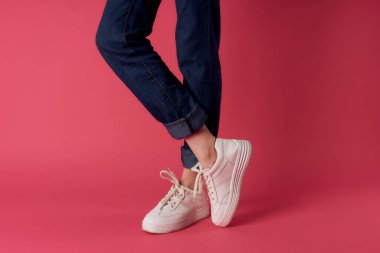 Kadın ayakları, beyaz spor ayakkabıları, sokak moda, pembe arka plan.