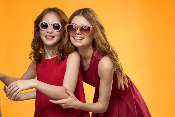 Cheerful fashionable family mom and daughter with sunglasses yellow background