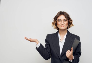 Belgeli bir iş kadını, elleri arka planda ve yüzünde gözlüklerle el kol hareketi yapar.