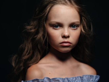 Gelinlik giymiş bir kız koyu bir arka plana karşı sert bir şekilde ileriye bakıyor.