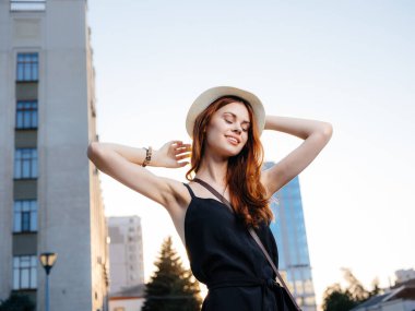 Gün batımında caddenin yanındaki binanın yanında siyah elbiseli zarif bir kadın.