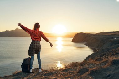 Elleri havada, gün batımında geriye bakan kadın turist.
