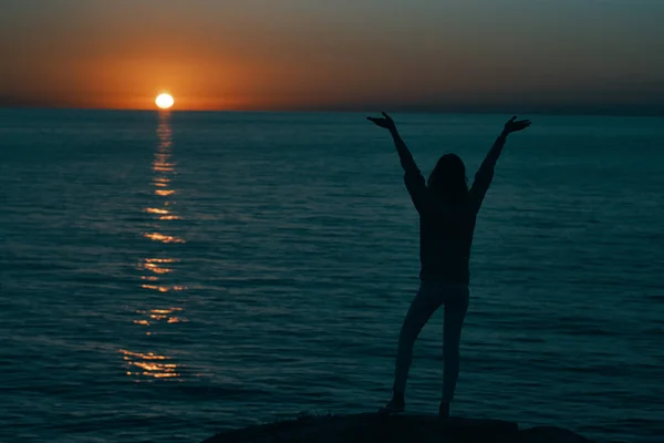 Mulher nas montanhas ao pôr do sol perto do mar levantou as mãos — Fotografia de Stock