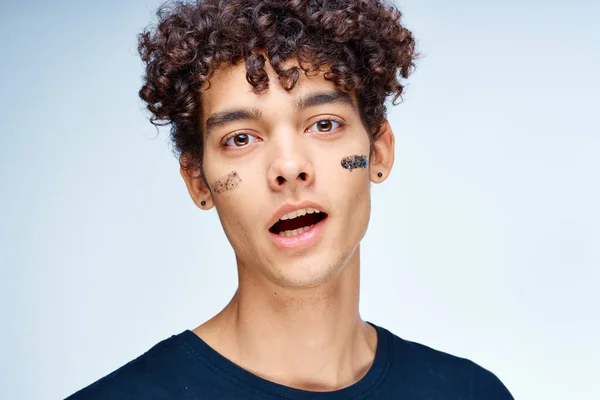 Guy with curly hair applies a black mask on his face cosmetology — Stock Photo, Image