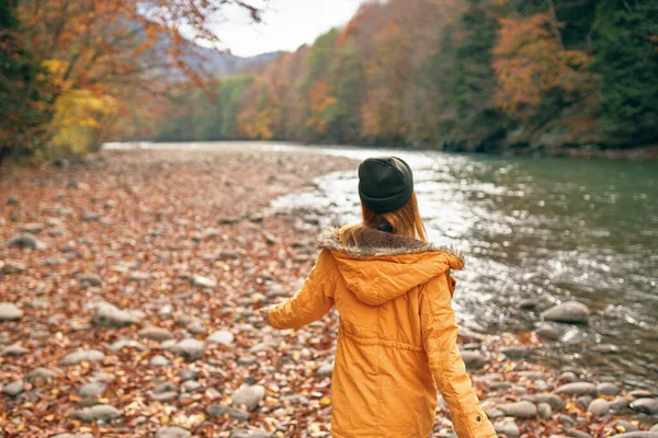 Vrouw in een geel jasje bij de rivier in de natuur herfst reizen — Stockfoto