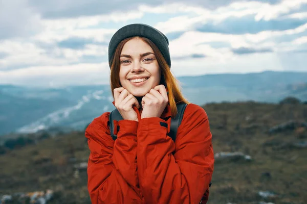 배낭을 찬 빨간 재킷을 입고 신선 한 공기가 흐르는 모자 산에 있는 행복 한 여자 — 스톡 사진
