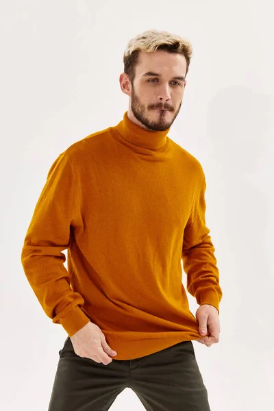 Blonder Mann mit orangefarbenem Pullover auf hellem Hintergrund und dunkler Hose — Stockfoto
