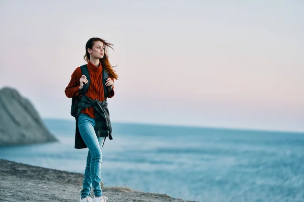 Woman in jeans with a backpack on her back sea in the background and high mountains — Stock Photo, Image