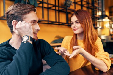 Bir kadın elleriyle hareket eder ve elinde saati olan yakışıklı bir adama bir şeyler söyler.