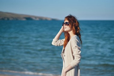 Kumsalda, yaz tatilinin yanında paltolu ve tişörtlü kızıl saçlı bir gezgin.