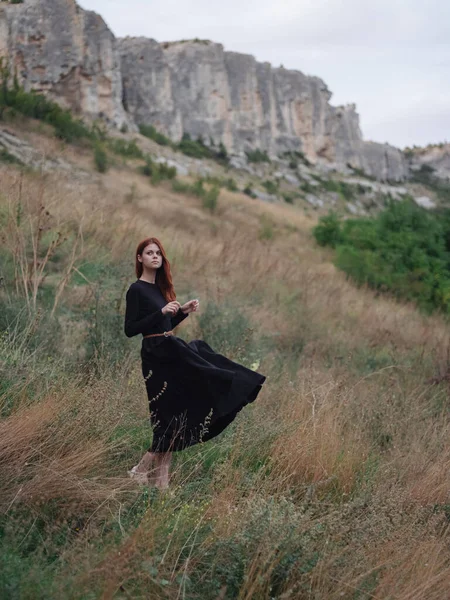 Mulher de vestido preto ao ar livre nas montanhas em um prado no outono — Fotografia de Stock